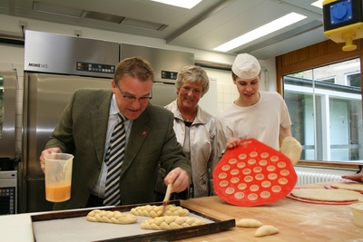 Regionspräsident Hauke Jagau (links) bestreicht Hefezöpfe für die Einweihungsfeier der neuen Schulbäckerei der Berufsbildenden Schule 2. Neben ihm: Schulleiterin Barbara Weichhold und der Auszubildende Stefan Reichert aus Gehrden