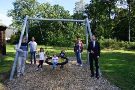 Joana Schwettlick, Lennya Schönhoff und Ciara Becker (Mitte, von links nach rechts) freuen sich über die neue Vogelnest-Schaukel. Mike Zimmermann und Karola Thielking (im Hintergrund links und rechts), Leitung Isy 7, bedankten sich mit Frank Engelhard, Geschäftsführer des Vereins Jugendzentrum Espelkamp e.V., bei André General (rechts), Zentralbereichsleiter Personal bei der HARTING Technologiegruppe