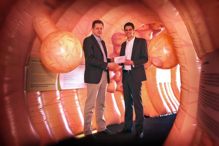 Dr. Henrik Mertens, leitender Betriebsarzt und Felix Farrenkopf, betrieblicher Gesundheitsmanager bei Heraeus mit dem Darmkrebsvorsorgetest im größten begehbaren Darmmodell Europas