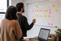 Zwei Personen planen an einem Whiteboard einen Redaktionskalender für Social-Media-Beiträge. Zwei Personen stehen in einem Büro vor einem Whiteboard mit einem handgeschriebenen Wochenplan für Social-Media-Beiträge, daneben ein Laptop mit geöffnetem Textentwurf. Symbolbild zur Organisation von Inhalten beim Einsatz von Künstlicher Intelligenz im Marketing.