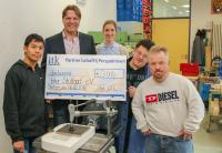 Stephan Schreiber von ITK Engineering (2. v. l.) überreicht Leonie Seidel und den Mitarbeitern des bhz Stuttgart e. V. den symbolischen Spendenscheck in der Abteilung „Kreativ & Industrie“ der Werkstatt Fasanenhof. (Foto: ITK Engineering)