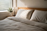 Frisch bezogenes Bett mit zwei Kopfkissen im Morgenlicht eines Schlafzimmers - Ein frisch bezogenes Bett mit zwei aufgeschüttelten Kopfkissen und zurückgeschlagener Decke, durch die halb geöffnete Jalousie fällt Morgenlicht auf das Kopfende. Symbolbild zur Schlafdauer von Erwachsenen in Deutschland und zur Ausstattung des Schlafplatzes