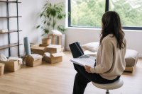 Physiotherapeutin richtet ihre neue Praxis ein und prüft Unterlagen. Eine Frau in einem noch halb eingerichteten Praxisraum sitzt auf einem Hocker, vor sich ein Laptop und Papierunterlagen, im Hintergrund unausgepackte Kartons. Symbolbild zu freiberuflichen Existenzgründungen in Deutschland.