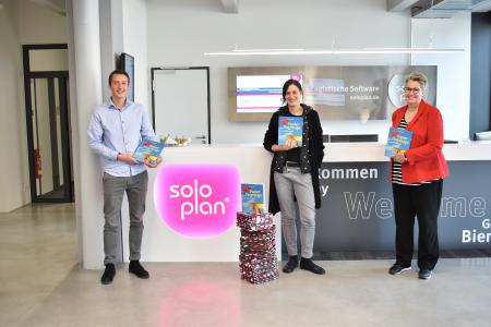 Conny Roth (Mitte) und Regine Bücker (rechts) vom Kinderschutzbund Kempten e.V. mit Christoph Breher (Soloplan) bei der Übergabe der Bastelbücher in Soloplan City.