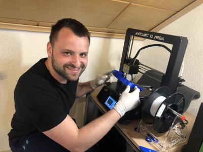 Patrick Grub druckt in der heimischen Werkstatt mit seinen 3D-Druckern die Halterungen für Face Shields, die wie Atemschutzmasken gerade dringend gebraucht werden / Bildnachweis: © Hochschule Aalen | Patrick Grub