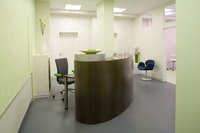 Der Empfangsbereich der Praxis präsentiert sich in zarter, frischer Farbigkeit. Der dunkle, organisch geformte Tresen steht entschieden und selbstbewußt frei im Raum.