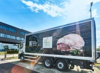 Ein EDEKA SÜDWEST FLEISCH / HOFGLÜCK Kühl-Lkw mit einem Bild von rohem Fleisch auf der Seite steht auf einem Parkplatz vor einem modernen Gebäude.
