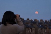 Person beobachtet den Mond am frühen Morgen mit einem Fernglas