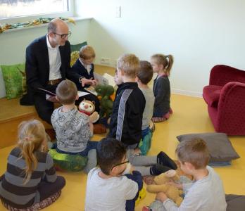 Robert Langhans, kaufmännischer Leiter von Piening Personal, liest acht Kindern der Fuchs Gruppe „Geschichten der freundlichen Drachenfamilie“ vor / Quelle: Piening Personal