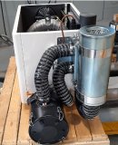 Die Abbildung zeigt eine industriell ausgeführte Schallschutzkabine, die auf einer Holzpalette vormontiert ist. Hinter der Kabine ist ein Seitenkanalverdichter positioniert, der über einen flexiblen Verbindungsschlauch mit einem zylinderförmigen Filtermodul verbunden ist. Auf der gegenüberliegenden Seite der Kabine befindet sich ein schallgedämmter Luftauslass mit angeschlossenem Schalldämpfer. Sämtliche Schlauchverbindungen sind mit Metallklammern fixiert.