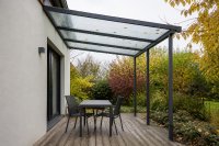 Freistehende Terrassenüberdachung aus Aluminium und Glas an einer Hauswand im Herbstlicht