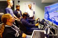 Artur Barz benutzt den Fahrsimulator mit der VR-Brille, neben ihm sitzt Tobias Puderer. Das Experiment beobachten Prof. Jan Conrad, Andreas Weisenberg und Patrick Schmitt (von links). Foto: Susanne Lilischkis