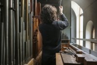Orgelbauer arbeitet an einer geöffneten Pfeifenorgel auf der Empore