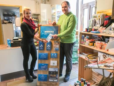 WEMAG-Mitarbeiterin Johanna Möller und Ladeninhaber Henrik Lemcke (v.l.) bestücken den Aufsteller im Dorfladen Demen mit Informationsmaterial für Strom- und Erdgaskunden / Foto: WEMAG/Sebastian Kosog