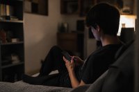 Jugendliche sitzt abends mit Smartphone auf dem Bett