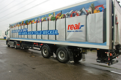 Transport und Werbung - alles mit einem LKW. Die neue Real Werbekampagne schildert mit einem Augenzwinkern Situationen aus dem täglichen Verkehrschaos