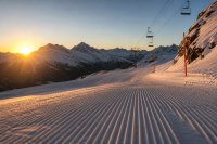 Eine frisch präparierte Skipiste im ersten Morgenlicht: orangefarbene Pistenmarkierungen am Rand, ein leerer Sessellift im Gegenlicht, dahinter verschneite Gipfel unter klarem Himmel. Symbolbild zur Unfallanalyse im alpinen Skisport vor der Wintersaison 2026/27.
