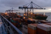 Ein Containerterminal in der Abenddämmerung: Reihen gestapelter Container, mehrere Portalkräne über der Kaikante und ein Frachtschiff, das gerade festmacht. Symbolbild zur Herbstprognose für Welthandel und Weltwirtschaft 2026.