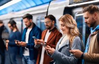 Eine Gruppe von Pendlern an einem Bahnsteig, vertieft in ihre Smartphones. Männer wie Frauen egal welchen Alters nutzen jede freie Sekunde, um ihren Newsfeed in sozialen Netzwerken zu checken.