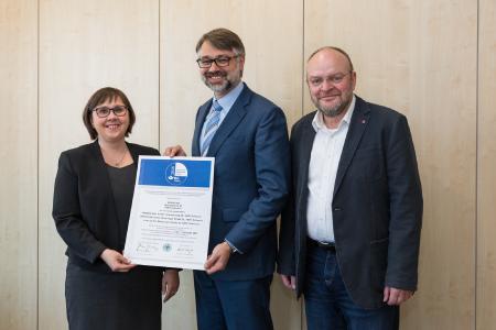 Margarita Schmidt von der Berufsgenossenschaft überreicht WEMAG-Vorstandsmitglied Thomas Murche und der Fachkraft für Arbeitssicherheit der WEMAG-Unternehmensgruppe, Roland Rohde, die Urkunde. Foto: WEMAG/Stephan Rudolph-Kramer