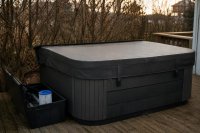 Abgedeckter Whirlpool auf einer Holzterrasse im späten Herbstlicht mit beschlagener Abdeckung. Ein geschlossener Whirlpool mit aufliegender Thermoabdeckung auf einer Holzterrasse, daneben ein Filterschacht mit geöffnetem Deckel, im tief stehenden Licht eines Herbstnachmittags. Symbolbild zur Wasserhygiene in privaten Whirlpools.