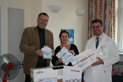 Stephan Schilling (Vorstand der Comline AG) übergibt Prof. Dr. Dominik Schneider (Leiter der Kinder- und Jugendmedizin) und Susanne Dobbelmann (stellvertretende Leiterin der Spieleinsel) die Spende