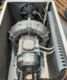 Das Bild zeigt einen eingebauten Seitenkanalverdichter vom Typ K05MS-1,1-3ph-ATEX II 3GD innerhalb einer schallgedämmten Schutzkabine (Modell 25IH5). Der Verdichter ist vibrationsentkoppelt montiert und mit flexiblen Anschlussleitungen versehen. Im Hintergrund sorgt ein großdimensionierter Lüfter für die notwendige Kühlluftzufuhr. Die Kabelzuführung erfolgt strukturiert über einen integrierten Kabelkanal.