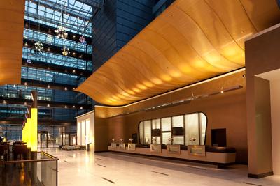 Weit aufschwingende Flügel akzentuieren die Rezeption im luftigen Atrium der großen Hotel-Lobby. Ergänzt wird die empfangende Geste durch golden schimmernde Rückwände, beschichtet mit Capadecor Metallocryl / Foto: JOI-Design, Hamburg
