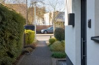 Der Eingangsbereich eines Reihenhauses am Nachmittag: eine Haustür mit Klingeltableau und Briefkasten, davor ein kurzer Plattenweg durch den Vorgarten bis zum öffentlichen Gehweg, links die Hecke zum Nachbargrundstück, geparkte Autos am Straßenrand unscharf im Hintergrund. Symbolbild zum Erfassungsbereich von Klingelkameras.