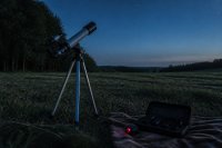 Aufgestelltes Linsenteleskop auf einer Wiese am Rand eines Waldes in der Abenddämmerung
