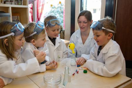 In einem Experiment spüren die Kinder des Kindergartens Schalchen (v.li.n.re.) Amelie Kogler, Dominik Junghuber, Alexander Moser und Paul Wallner gemeinsam mit Kindergartenpädagogin Maria Zauner den Eigenschaften des Germs nach. Vermischt mit Zucker, Mehl und warmem Wasser wird ein über eine Flasche gestülpter Ballon langsam aufgeblasen / Foto: Chris Hofer