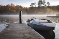 Ein Holzsteg in einem Yachthafen am Bodensee im Oktober, am Stegende eine schlanke Ladesäule mit eingestecktem Kabel, daneben ein vertäutes kleines Elektro-Sportboot, ruhiges Wasser, Herbstlicht und Nebel über dem See. Symbolbild zu eFoils und Elektroantrieben auf dem Wasser. Bild KI-generiert.