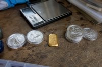 Silbermünzen und ein Goldbarren liegen nebeneinander auf einer Werkbank
