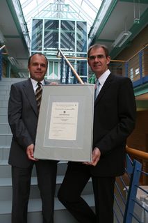 Stolz präsentieren der Institutsleiter Dr.M.Bastian(re) und Dipl.-Ing.R.Schmitt die von der Trägergemeinschaft für Akkreditierung erhaltene Akkreditierungsurkunde für die ‚Zertifizierung von Arbeitssicherheitsmanagement-systemen nach OHSAS