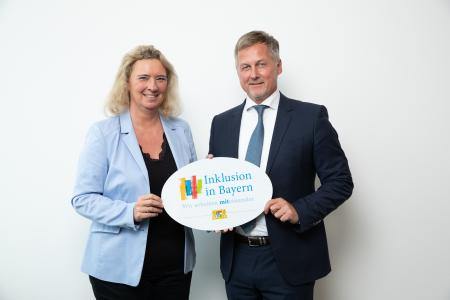 Kerstin Schreyer (links), Staatsministerin für Familie, Arbeit und Soziales, übergibt das Emblem „Inklusion in Bayern – Wir arbeiten miteinander!“ an Dieter Hahn, Managing Director der auticon GmbH