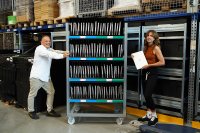 Zwei Mitarbeitende von AfB social & green IT, die im Produktionsbereich neben einem der mobilen Notebookwägen mit Geräten von EY festhalten.
