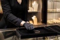 Verkäuferin legt ein Schmuckstück in einer Boutique auf ein Samttablett. Eine Verkäuferin legt in einer hochwertig eingerichteten Boutique ein Schmuckstück auf ein Samttablett, im Hintergrund unscharf beleuchtete Vitrinen. Symbolbild zur Entwicklung des weltweiten Luxusmarkts und zur führenden Rolle der Kategorie Schmuck. Bild KI-generiert