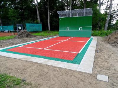 Der Unterbau der kleinen Tennis-Anlage wurde aus frostsicherer und verdichteter Schotterschicht, einem Planum aus Edelbruch 0/2 Pflastersand, sowie einem 12 mm starken Gummibelag, hergestellt. Der Gummibelag verhindert den Durchwuchs von Gräsern, leitet das Regenwasser in die zuvor installierte Drainage ab und gibt dem Tennisbelag eine elastische Fläche gegen Sportverletzungen.