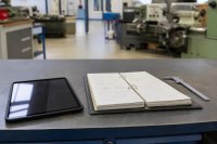 Werkbank in einer Ausbildungswerkstatt mit Tablet und aufgeschlagenem Ordner