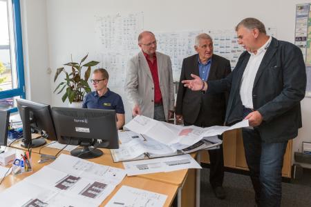 Am Arbeitsplatz von Objektkalkulator Christian Fiedler (li.) erläutert Unternehmer Jürgen Kuhnert Pampows Bürgermeister Hartwig Schulz und WEMACOM-Projektleiter Rainer Killer (v. re.) die Vorteile der Glasfaser-Internetverbindung: Die Fertigungspläne können nun in kürzester Zeit übertragen werden. Foto: WEMAG/Stephan Rudolph-Kramer