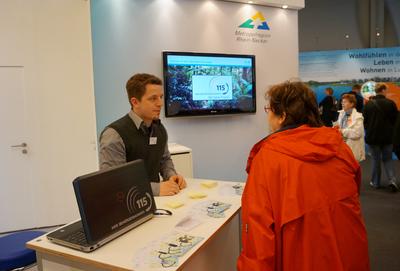 Mit verschiedenen Maßnahmen wird die einheitliche Behör-dennummer bekannt gemacht, hier mit einem Infostand beim Mannheimer Maimarkt 2013, Foto: Metropolregion Rhein-Neckar GmbH