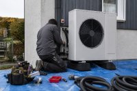 Monteur schließt eine Wärmepumpe an der Außenwand eines Wohnhauses an