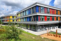 Die markante, vielfarbige Ummantelung des neuen Kinderzentrums besteht aus maßgefertigten Verschalungselementen, die sich passgenau ineinanderfügen. Die Pfosten-Riegel-Fassade von Schüco ermöglicht großformatige Fensterelemente, die ein Maximum an Tageslicht hereinlassen.