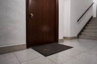 Geschlossene Wohnungstür in einem Treppenhaus mit Schlüsselbund auf der Fußmatte. Eine geschlossene Wohnungstür mit Zylinderschloss in einem schlicht gefliesten Treppenhaus, davor liegt ein Schlüsselbund auf der Fußmatte, das Licht kommt aus einer Deckenleuchte. Symbolbild zum Schlüsselnotdienst und zu den Kosten einer Türöffnung.