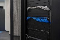 Ein Netzwerkschrank mit sorgfältig geordneten Patchkabeln und beschriftungsfreien Feldern steht in einem Technikraum. Symbolbild zu organisatorischen Pflichten der IT-Sicherheit. Bild KI-generiert.