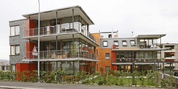 Große Südfenster, leuchtend orange Putzflächen und grüne Schiefer an Dach und Wand prägen das Mehrfamilienhaus in Thalwil