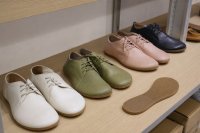 Mehrere Paar flache Schuhe mit dünner Sohle auf einem Holzregal in einem Schuhgeschäft. : Auf einem hellen Holzregal in einem Schuhgeschäft stehen mehrere Paar flache Schuhe mit breiter Zehenbox und dünner, biegsamer Sohle in verschiedenen Farben, daneben liegt eine einzelne Sohle zur Ansicht. Symbolbild zu Barfußschuhen im Fachhandel.