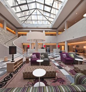 Die in Metallglanzeffekte getauchte Lobby mit ihrer überdimensionalen Tischlampe im Mittelpunkt beeindruckt genauso wie die Gestaltung des schwungvollen Treppenaufgangs im Hintergrund (Foto: Alligator/DAW)